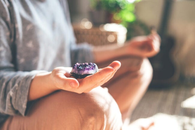 woman meditating with purple crystal in her hand