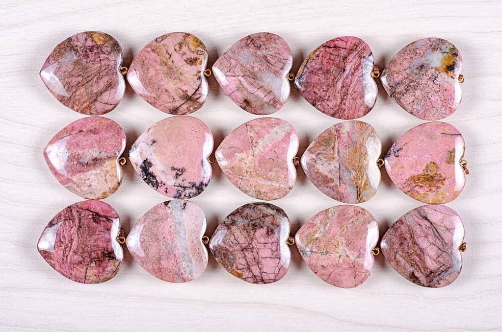 Fifteen rose-pink rhodonite heart-shaped stones are stowed three rows. Five pieces in each one. Top view.