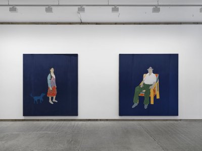 View of a gallery with two artworks both with blue backgrounds hang on a wall. One shows a woman and dog and the other a seated man.