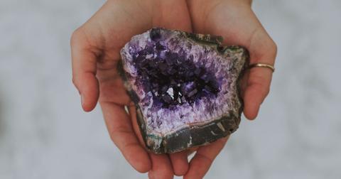Hands holding purple amethyst crystal