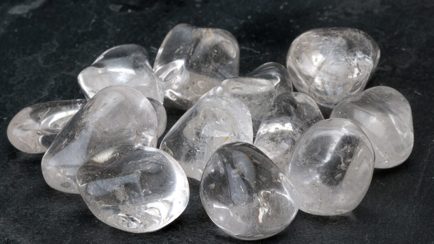 Clear Quartz polished tumblestones on dark slate background