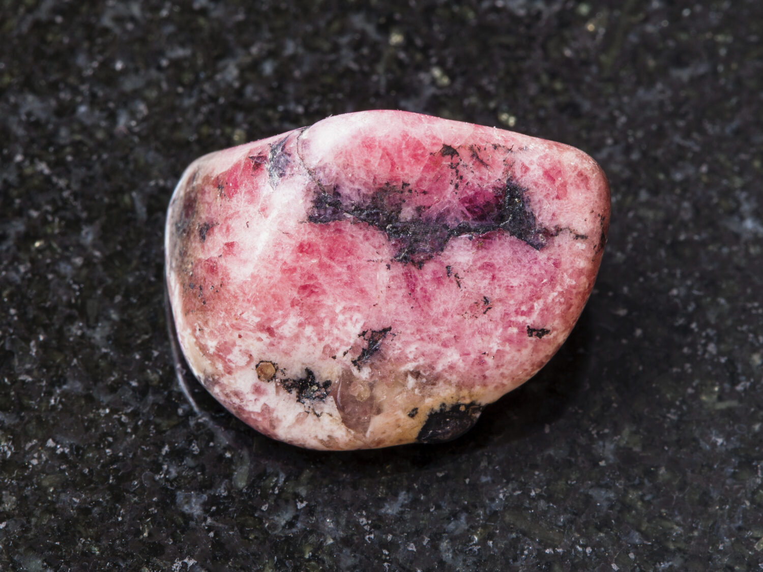 macro shooting of natural mineral rock specimen - polished pink rhodonite gem stone on dark granite background from Ural mountains in Russia