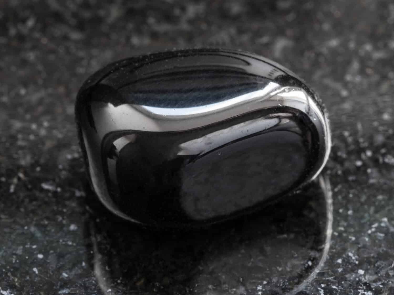 macro shooting of natural mineral rock specimen - polished black Onyx gemstone on dark granite background